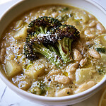 Creamy white bean and potato soup garnished with dark charred broccoli florets and freshly grated Parmesan