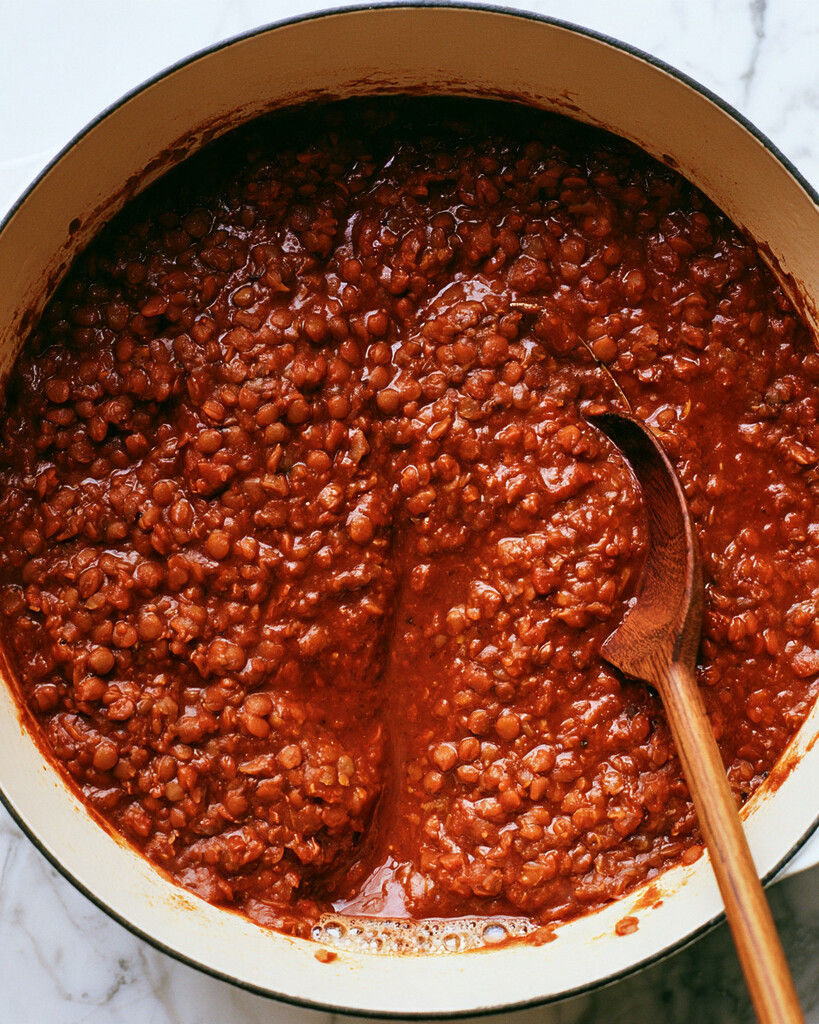 Thick red lentil bolognese simmering in a Dutch oven with tender whole lentils visible in the sauce