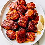 Glossy hot honey blackened air fryer salmon bites on an oval white platter with lemon wedges and honey drops