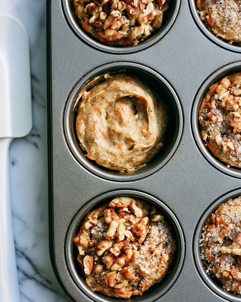 Thick carrot banana muffin batter scooped into metal muffin cups next to topped portions