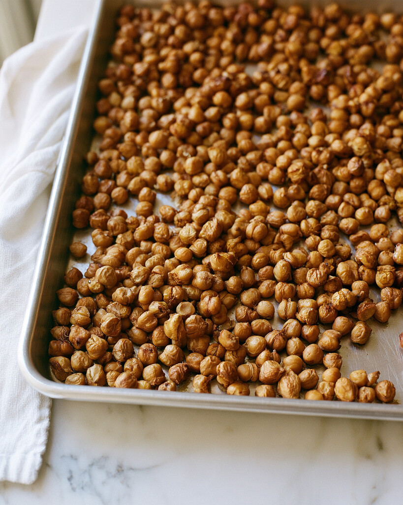 Golden-brown chickpeas with dry, wrinkled skins roasting on a metal baking sheet